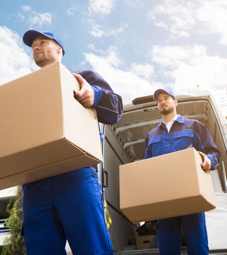 Zwei Männer in blauen Arbeitsanzügen transportieren Kisten.