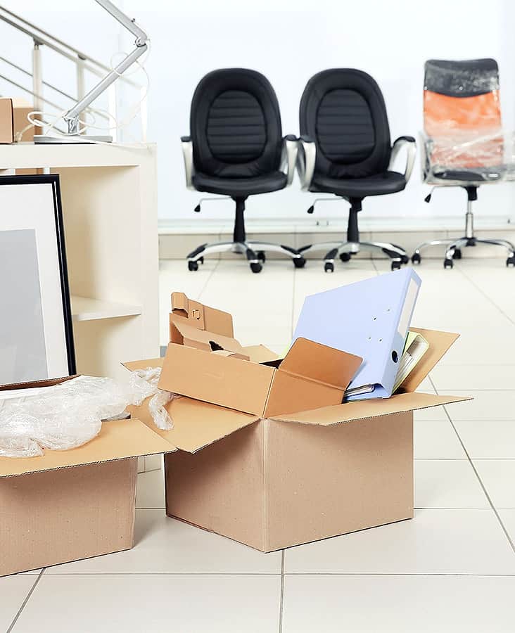 Umzugskartons und Stühle in einem Büro, die für einen bevorstehenden Umzug vorbereitet sind.