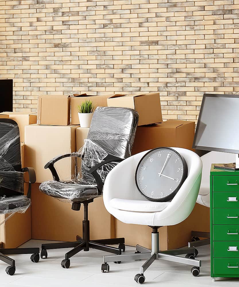 Büroeinrichtung in einem Raum, umgeben von Kisten und einer Wanduhr.